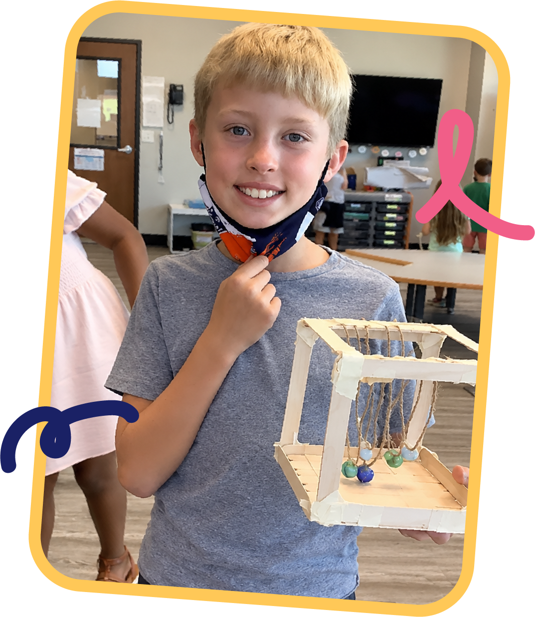 Smiling student holding a handmade Newton's cradle built from popsicle sticks and string, a STEM engineering project at STEM Bright Beginnings childcare and daycare in Leander, TX