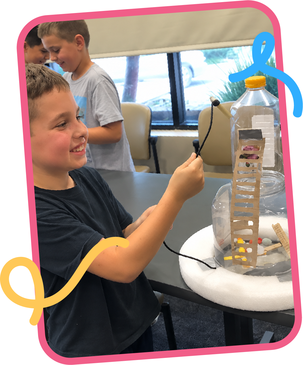 Smiling student demonstrating a DIY space capsule model built from a plastic bottle and cardboard, a STEM engineering project at STEM Bright Beginnings childcare and daycare in Leander, TX