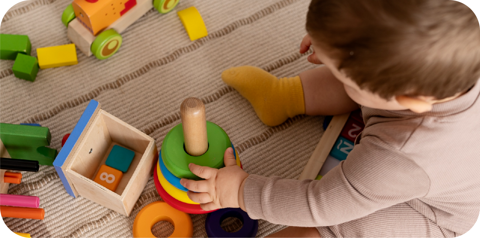 Infant playing with a wooden stacking ring toy surrounded by blocks and sensory toys in the Discoverers program at STEM Bright Beginnings in Leander, TX