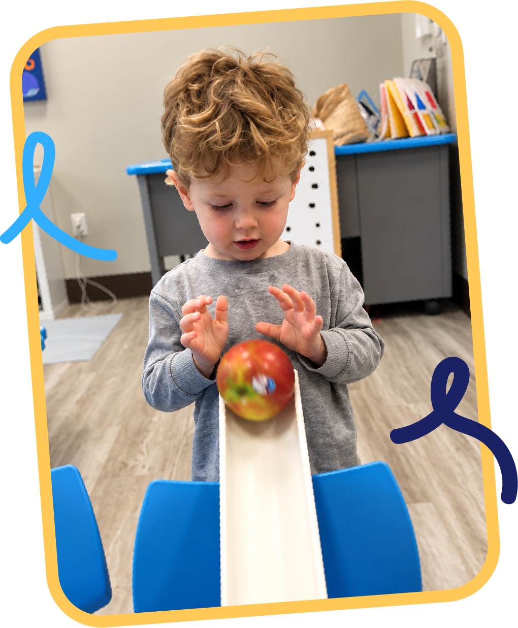 Young child exploring gravity and motion by rolling an apple down a ramp during a hands-on STEM activity at STEM Bright Beginnings childcare and daycare in Leander, TX